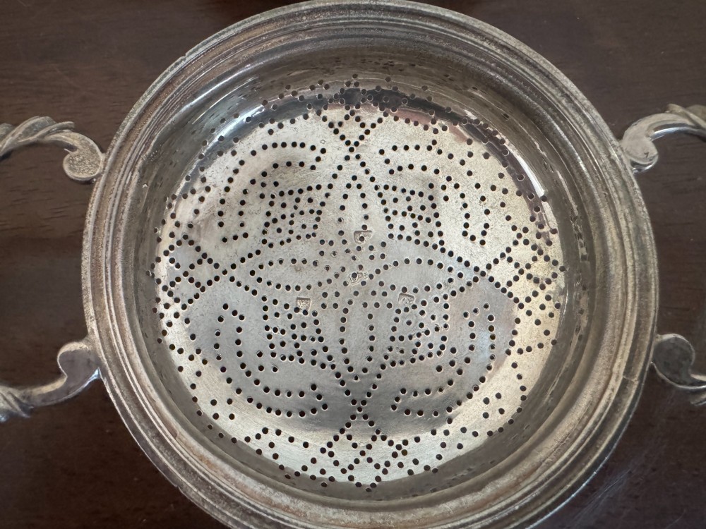 A matched pair of George III sterling silver lemon strainers featuring pierced geometric bowl patterns and dual side handles. View V
