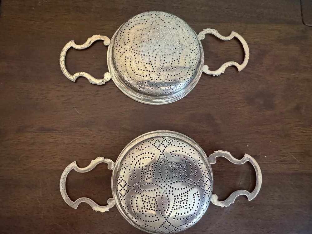 A matched pair of George III sterling silver lemon strainers featuring pierced geometric bowl patterns and dual side handles. View IX