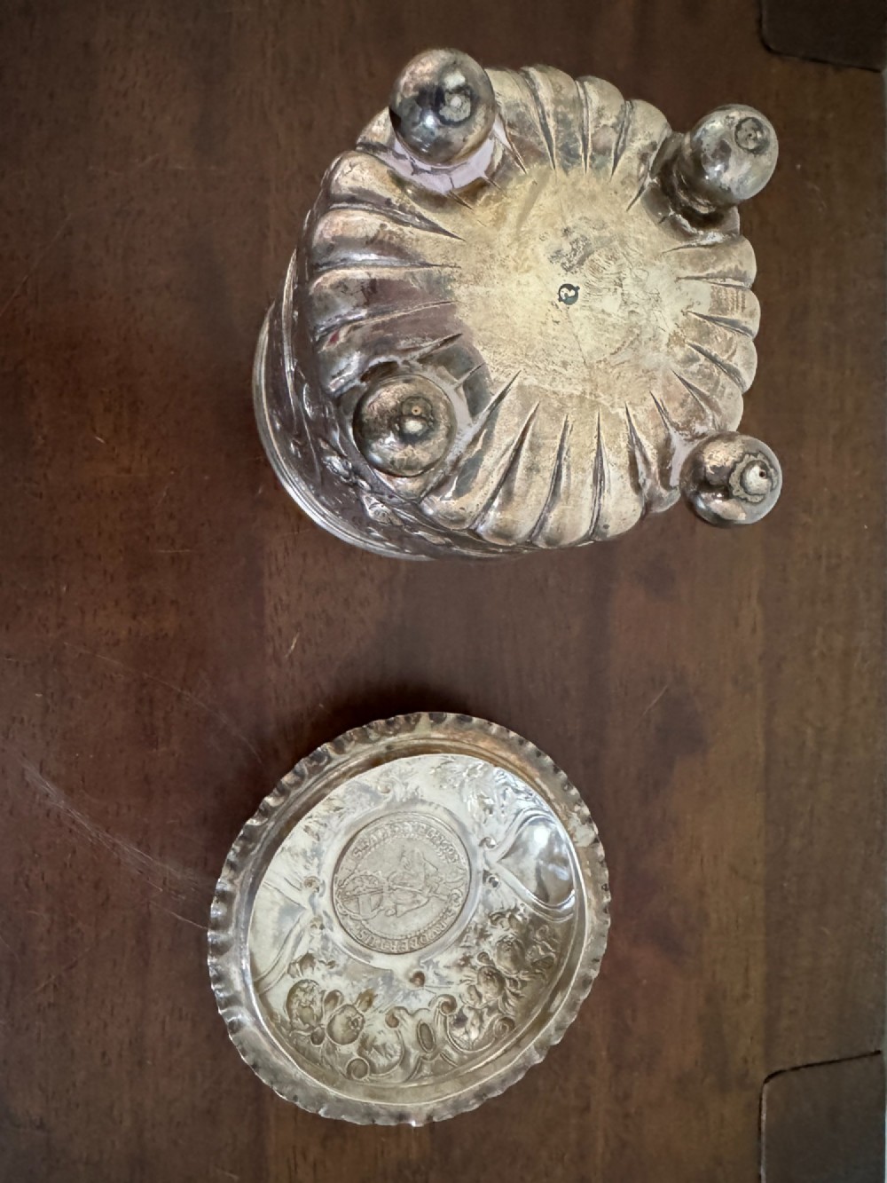 A sterling silver lidded beaker decorated with chased repousse scrollwork, embedded silver thaler coins, and standing on ball feet. View XII