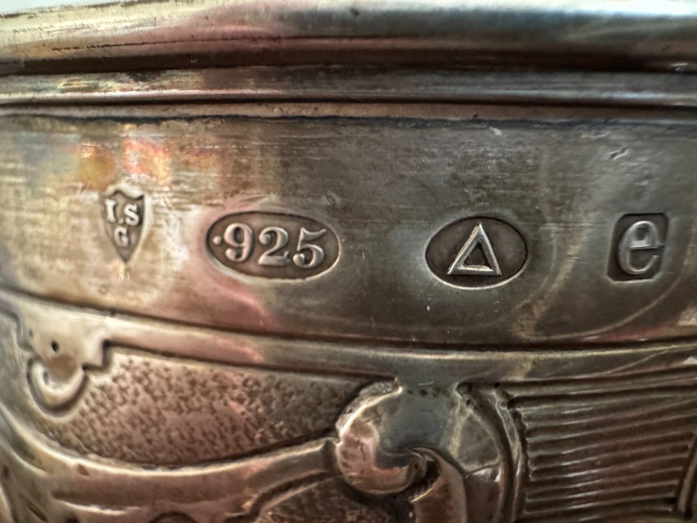 A sterling silver lidded beaker decorated with chased repousse scrollwork, embedded silver thaler coins, and standing on ball feet. View XIII