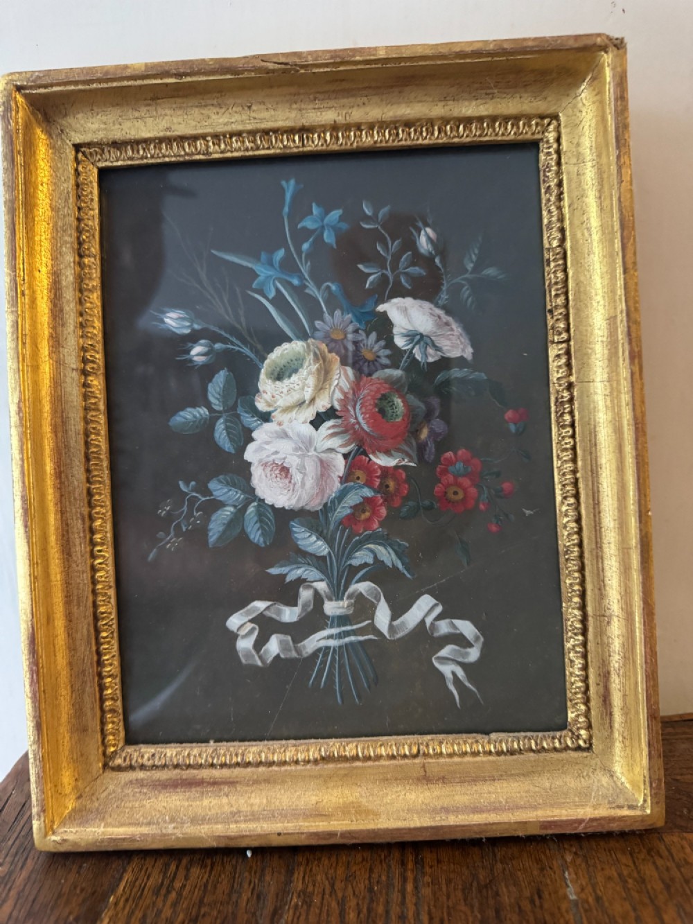 A pair of framed antique gouache paintings on dark backgrounds depicting floral bouquets tied with white ribbons, set in gilded frames. View V