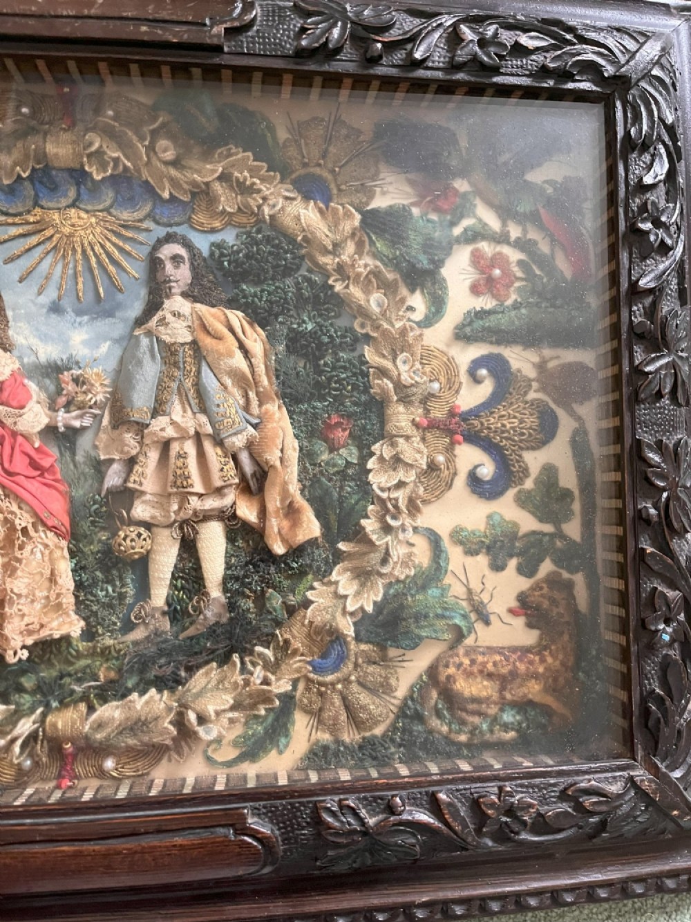 A 17th-century stumpwork embroidery picture depicting King Charles II and a lady in silk and metallic thread relief, set within a dark carved wooden frame. View III