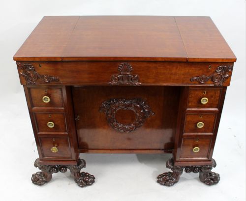 fig 1. Late 18th-century mahogany kneehole desk featuring carved lion paw feet, brass ring drawer handles, and a central cupboard door decorated with a carved laurel wreath.