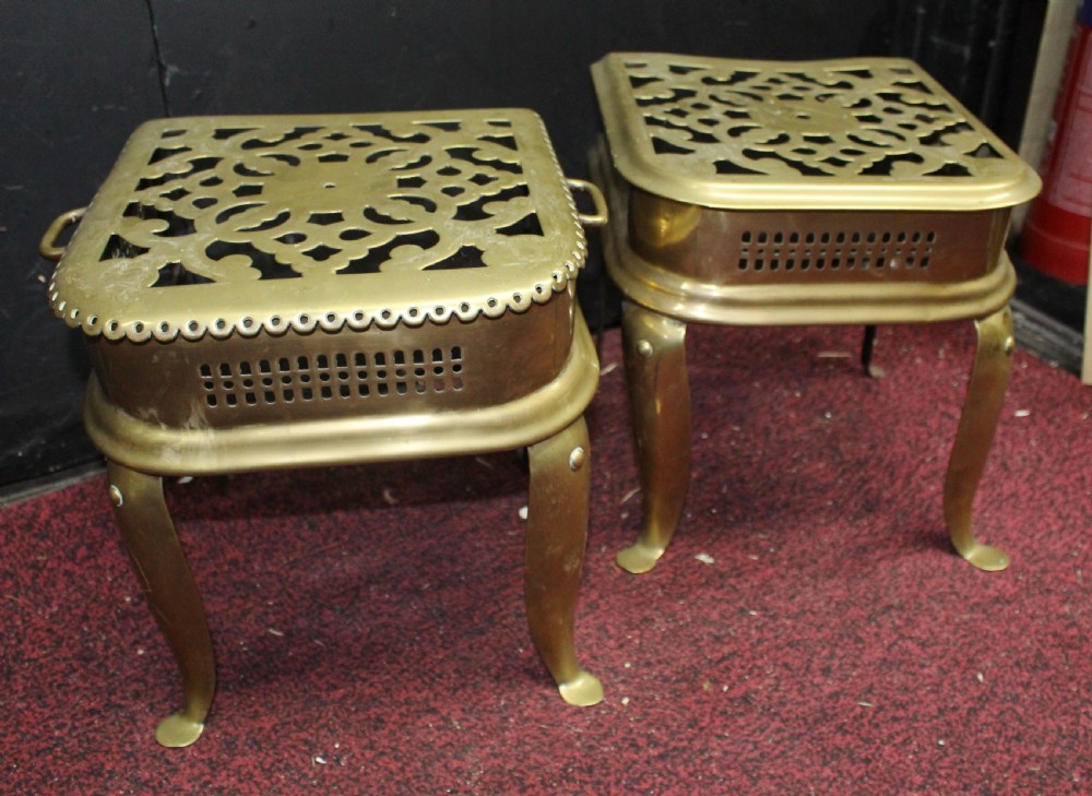 A pair of early 19th-century brass footman trivets featuring pierced lattice tops, side handles, and cabriole legs.