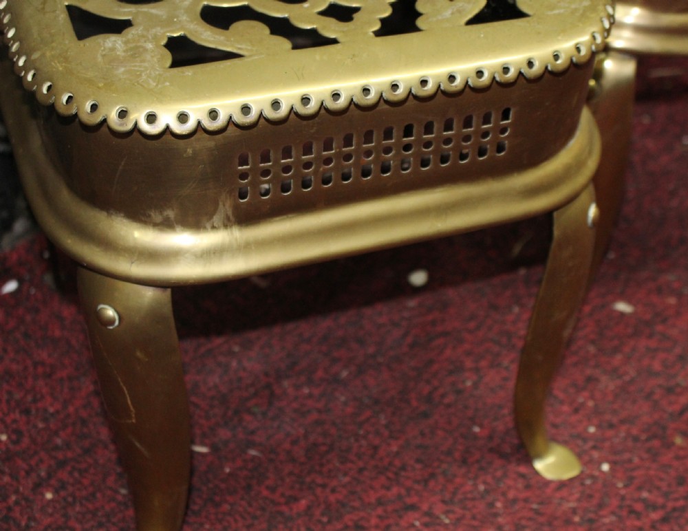 A pair of early 19th-century brass footman trivets featuring pierced lattice tops, side handles, and cabriole legs. View V
