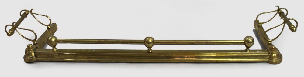 An antique solid brass low fireplace fender featuring a central tubular top rail with three spherical supports and elevated outswept tool rests on both sides.