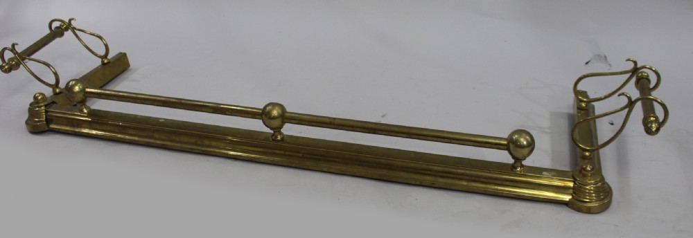 An antique solid brass low fireplace fender featuring a central tubular top rail with three spherical supports and elevated outswept tool rests on both sides. View II