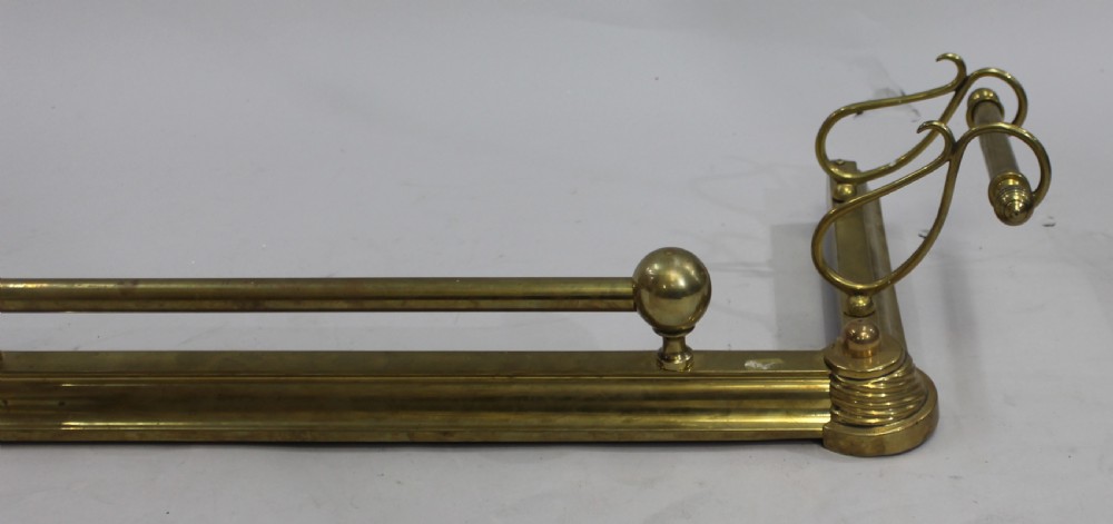 An antique solid brass low fireplace fender featuring a central tubular top rail with three spherical supports and elevated outswept tool rests on both sides. View III