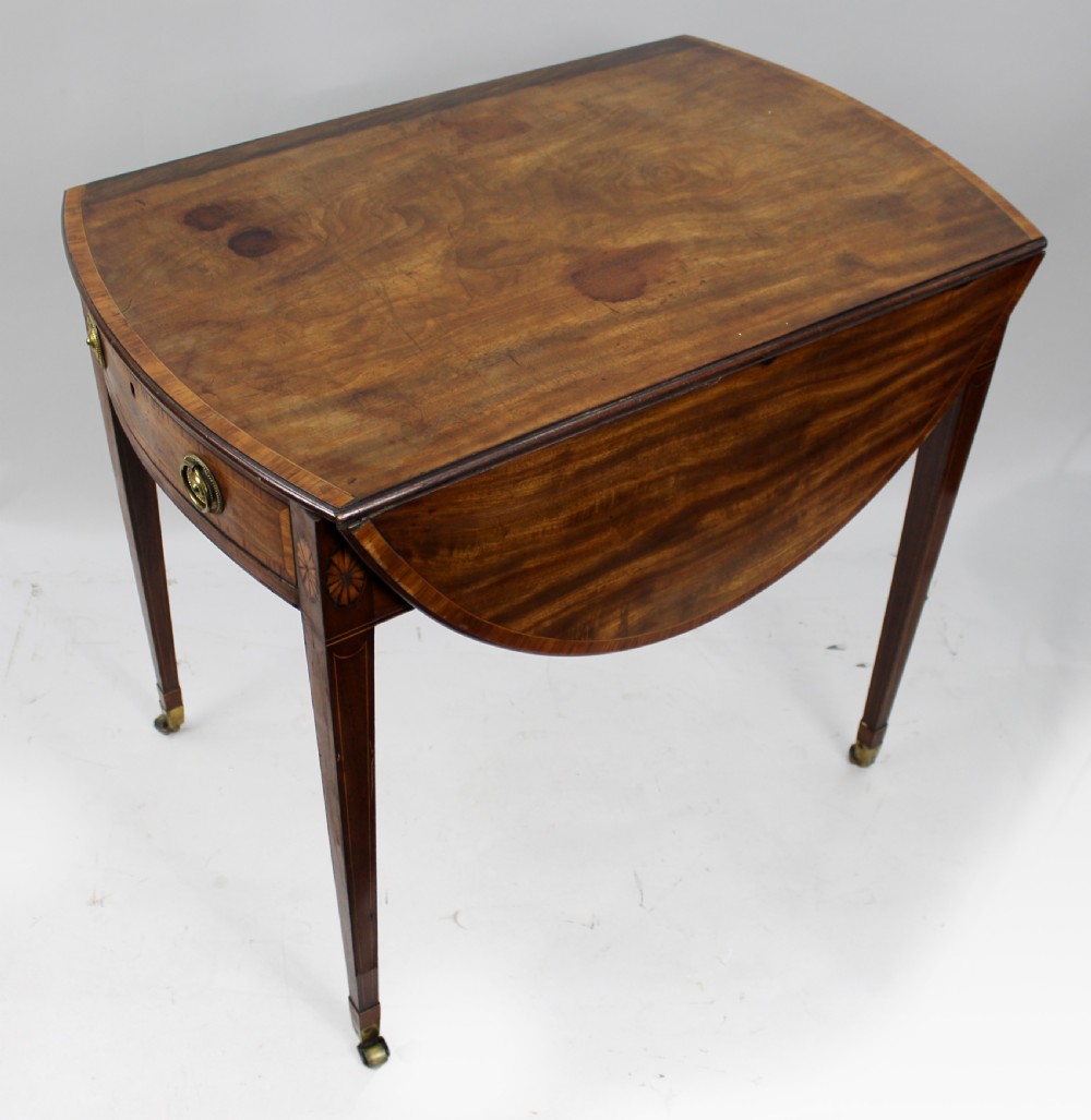 A George III mahogany Pembroke table featuring two hinged drop leaves, crossbanded inlay work, a single drawer with a brass ring handle, and square tapered legs with brass castors.