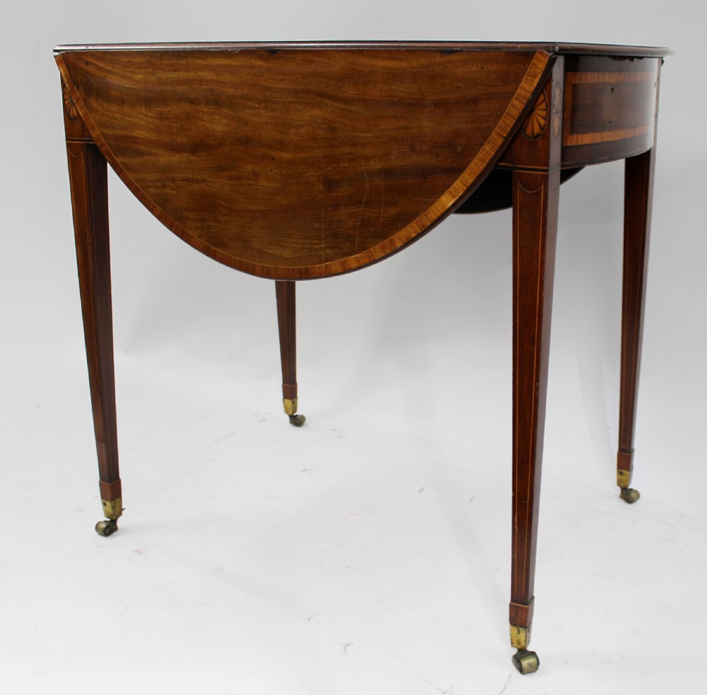 A George III mahogany Pembroke table featuring two hinged drop leaves, crossbanded inlay work, a single drawer with a brass ring handle, and square tapered legs with brass castors. View IV