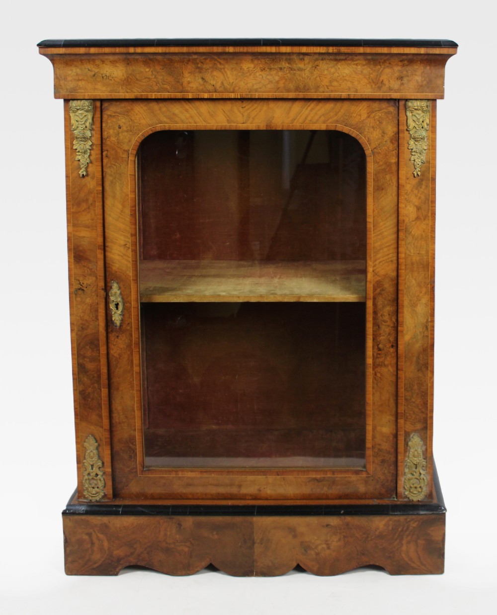 A Victorian burr walnut pier cabinet featuring a single glazed door, gilt-bronze mounts at the corners, an interior shelf, and a shaped plinth base.