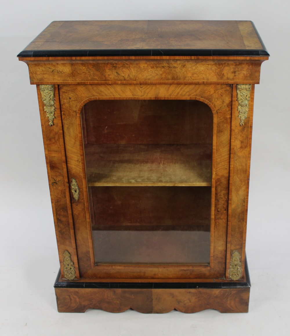 A Victorian burr walnut pier cabinet featuring a single glazed door, gilt-bronze mounts at the corners, an interior shelf, and a shaped plinth base. View II