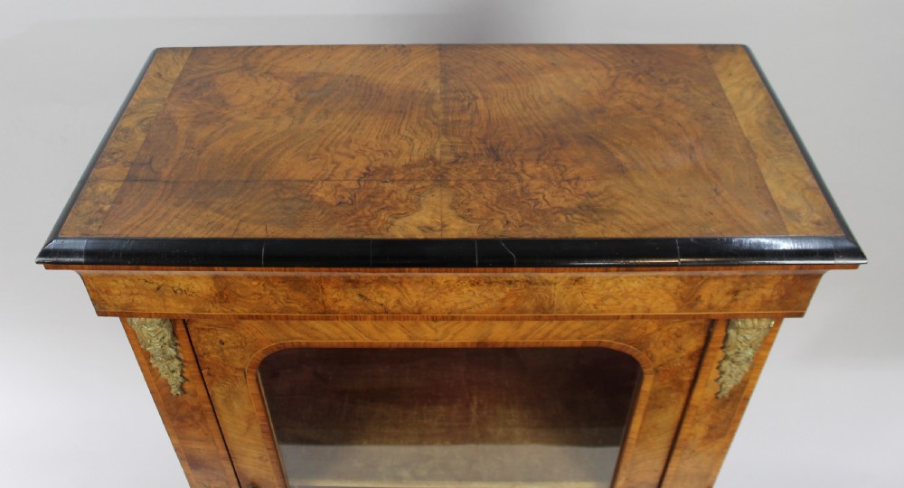 A Victorian burr walnut pier cabinet featuring a single glazed door, gilt-bronze mounts at the corners, an interior shelf, and a shaped plinth base. View III