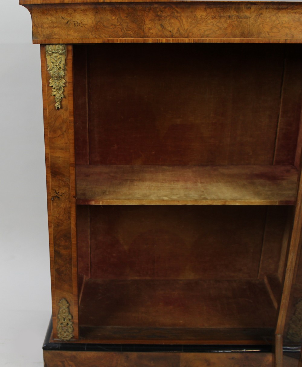 A Victorian burr walnut pier cabinet featuring a single glazed door, gilt-bronze mounts at the corners, an interior shelf, and a shaped plinth base. View V