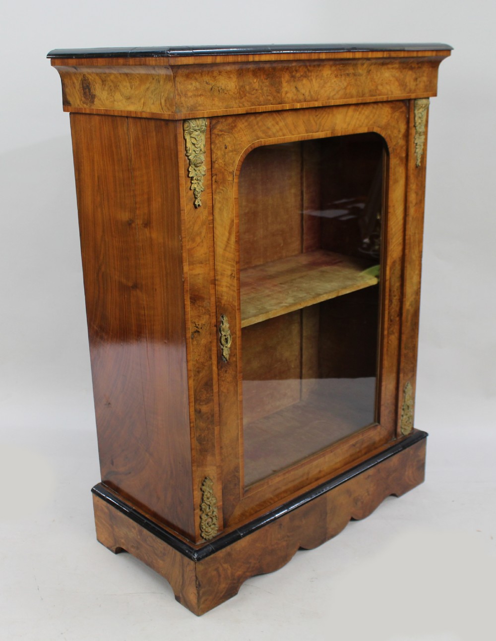 A Victorian burr walnut pier cabinet featuring a single glazed door, gilt-bronze mounts at the corners, an interior shelf, and a shaped plinth base. View VII