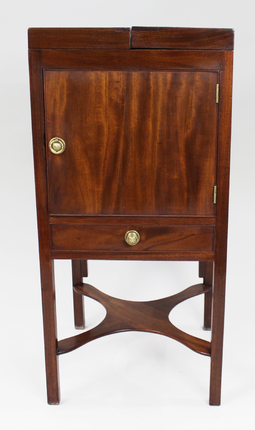 A George III mahogany vanity stand featuring a split folding top, a single cupboard door with a brass ring handle, a drawer, and an X-frame lower stretcher.
