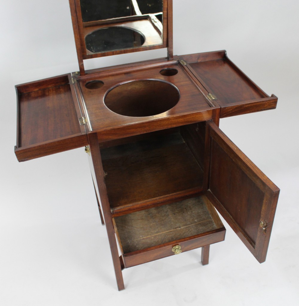 A George III mahogany vanity stand featuring a split folding top, a single cupboard door with a brass ring handle, a drawer, and an X-frame lower stretcher. View VII