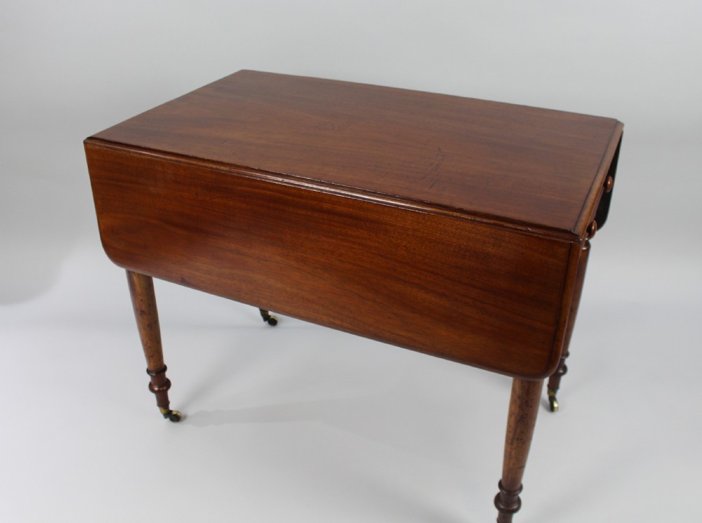 A Regency period mahogany Pembroke table featuring two drop leaves, a single end drawer with wooden turnings, four turned legs, and brass castors. View V