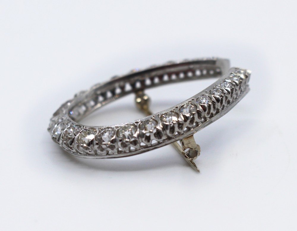 A platinum horseshoe-shaped brooch set with a graduating row of circular diamonds and fitted with a pin fastener on the reverse. View IV