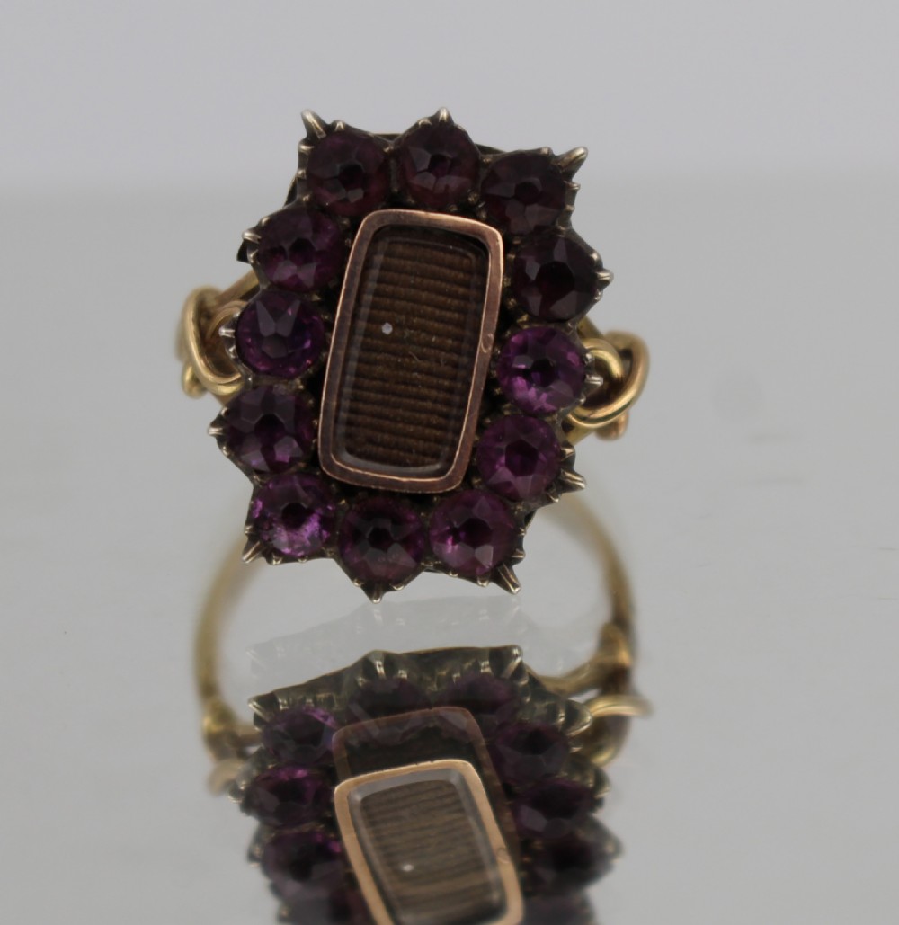 A Victorian gold mourning ring featuring a central rectangular compartment of woven hair surrounded by twelve purple glass stones.