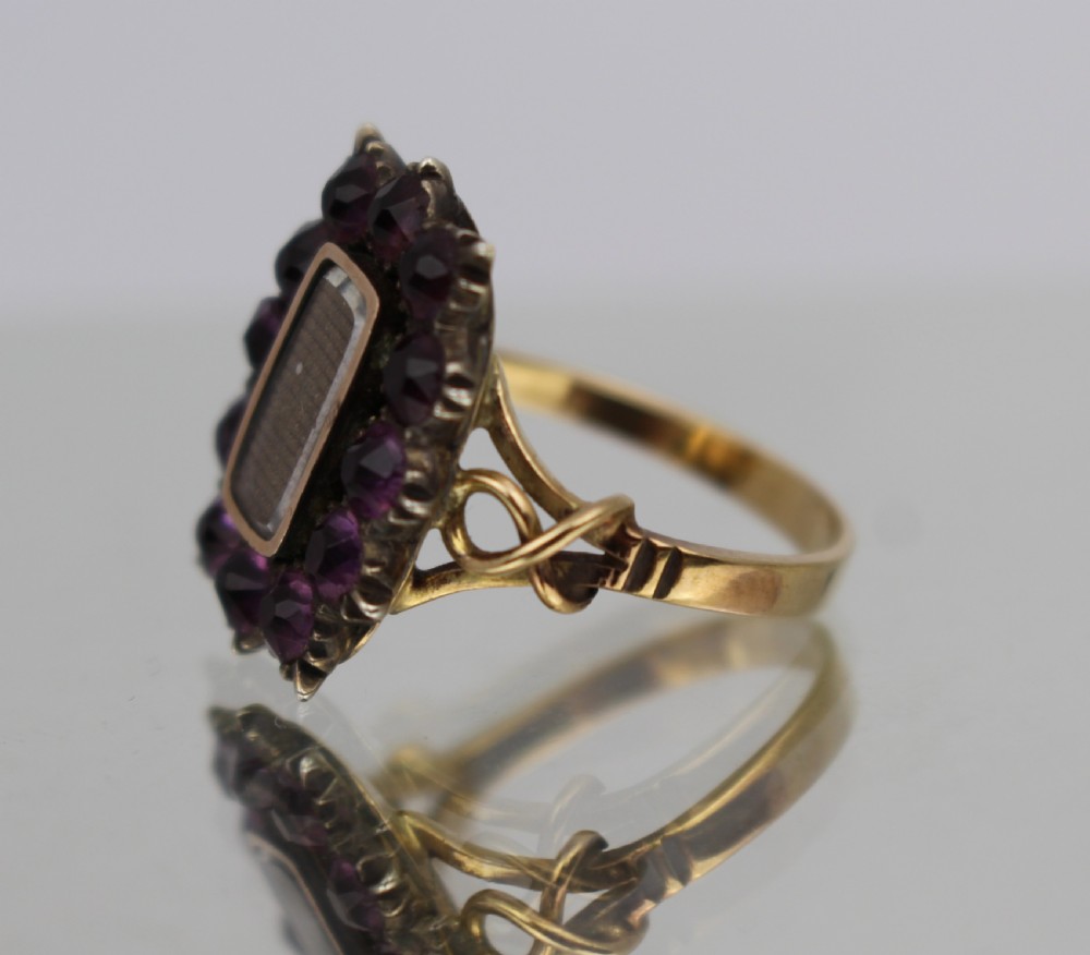 A Victorian gold mourning ring featuring a central rectangular compartment of woven hair surrounded by twelve purple glass stones. View II