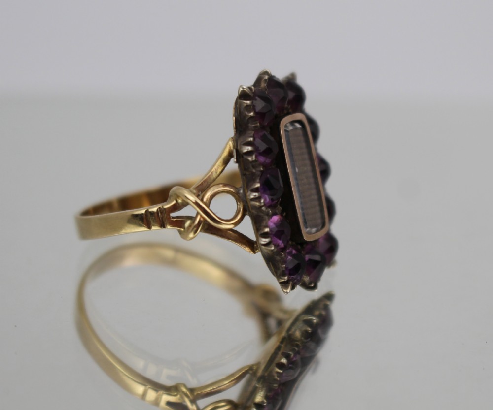 A Victorian gold mourning ring featuring a central rectangular compartment of woven hair surrounded by twelve purple glass stones. View V