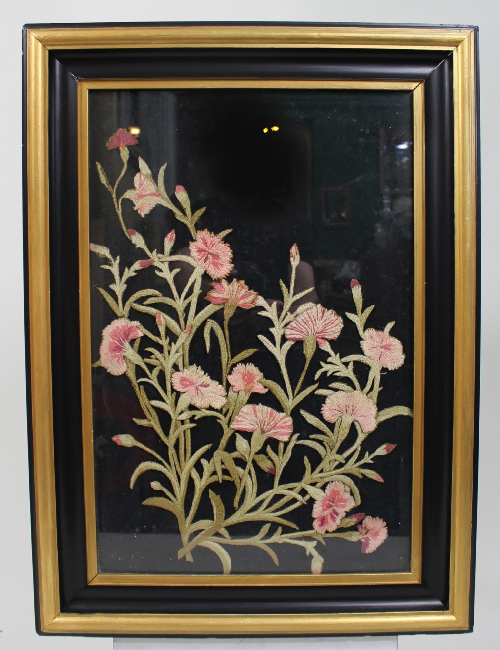 A framed Victorian needlework panel featuring embroidered pink floral motifs on a dark background within a black and giltwood frame.