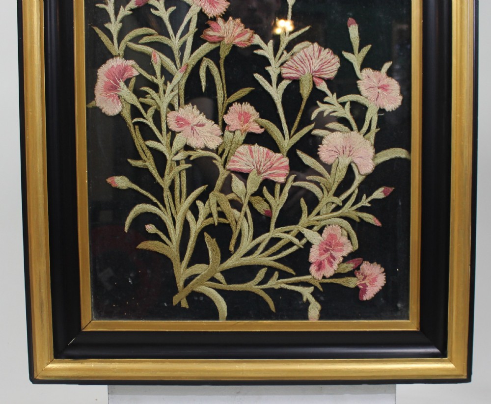 A framed Victorian needlework panel featuring embroidered pink floral motifs on a dark background within a black and giltwood frame. View II