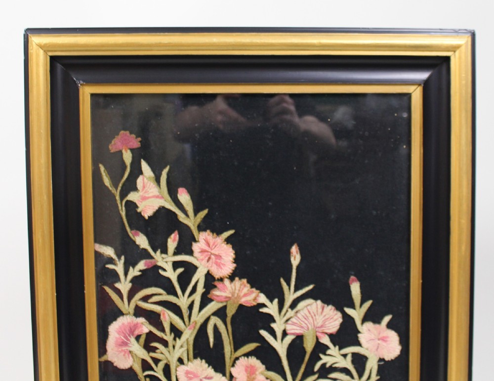 A framed Victorian needlework panel featuring embroidered pink floral motifs on a dark background within a black and giltwood frame. View III