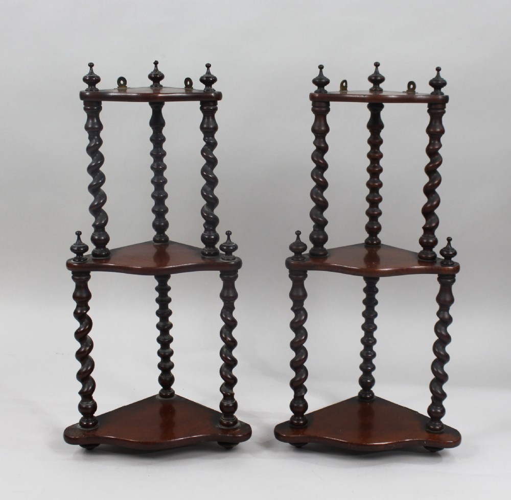 A pair of three-tiered dark mahogany corner shelves featuring barley twist turned pillars and top finials.