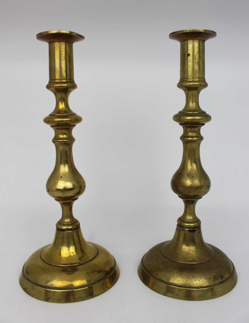 A pair of 19th-century brass candlesticks featuring turned baluster stems and rounded circular bases.