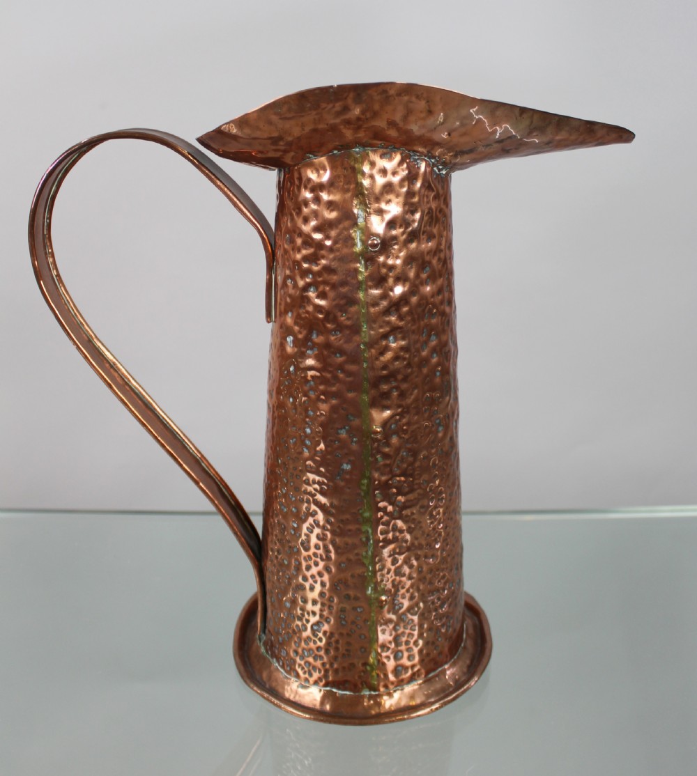 A hand-hammered copper jug featuring a flared spout and a large curved strap handle.