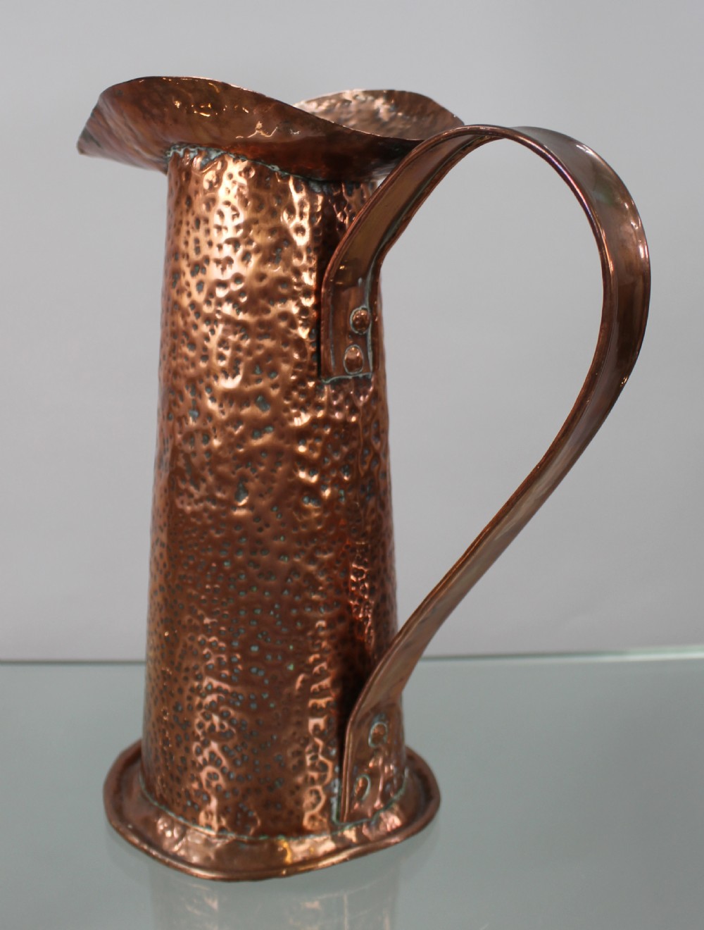 A hand-hammered copper jug featuring a flared spout and a large curved strap handle. View II