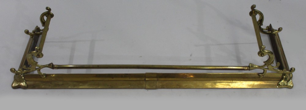 A Victorian brass fire fender with cast scroll end supports and a central horizontal rail resting on a low metal kerb. View II