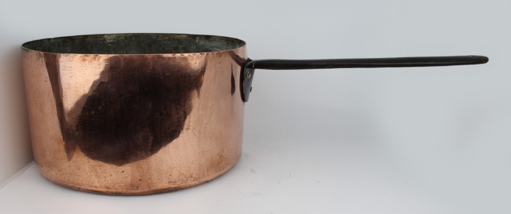 A large Georgian copper saucepan with a polished copper body, tin-lined interior, and a long black iron handle attached with rivets.