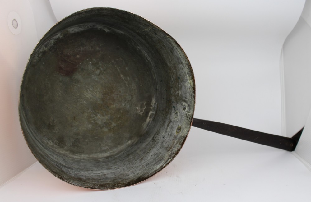 A large Georgian copper saucepan with a polished copper body, tin-lined interior, and a long black iron handle attached with rivets. View V