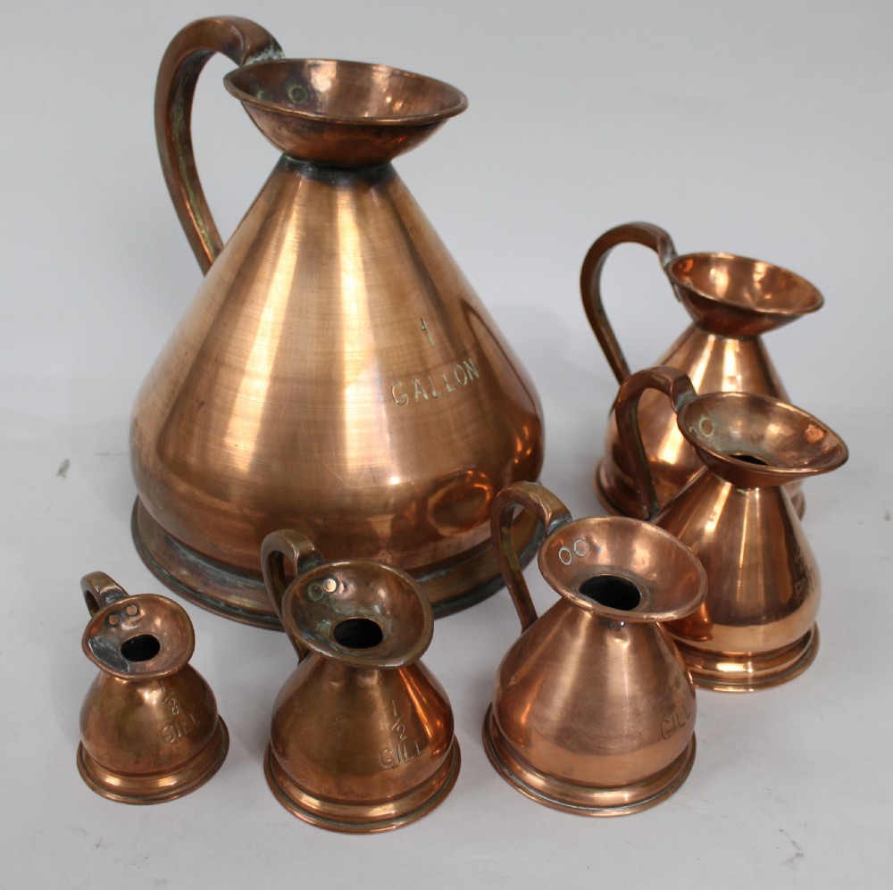 A set of six graduated antique copper haystack liquid measures ranging in size from one gallon down to one eighth gill, arranged on a plain background.