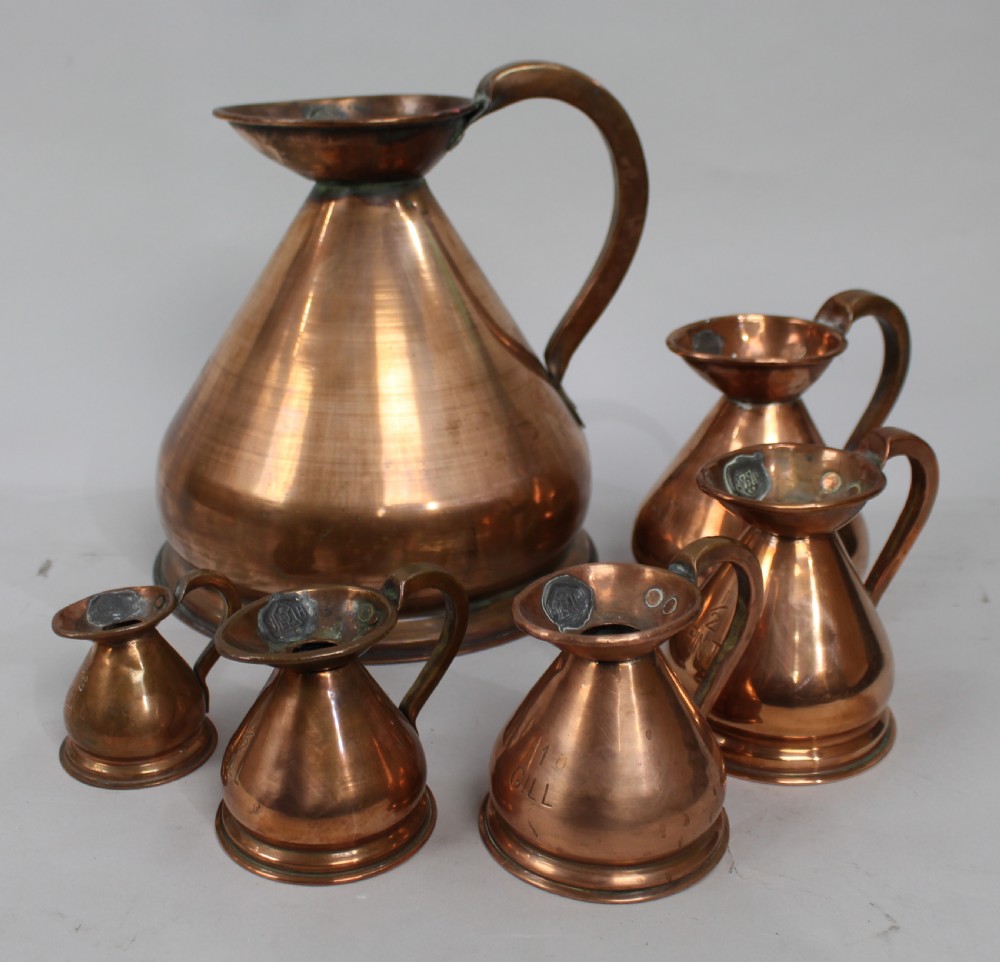 A set of six graduated antique copper haystack liquid measures ranging in size from one gallon down to one eighth gill, arranged on a plain background. View II