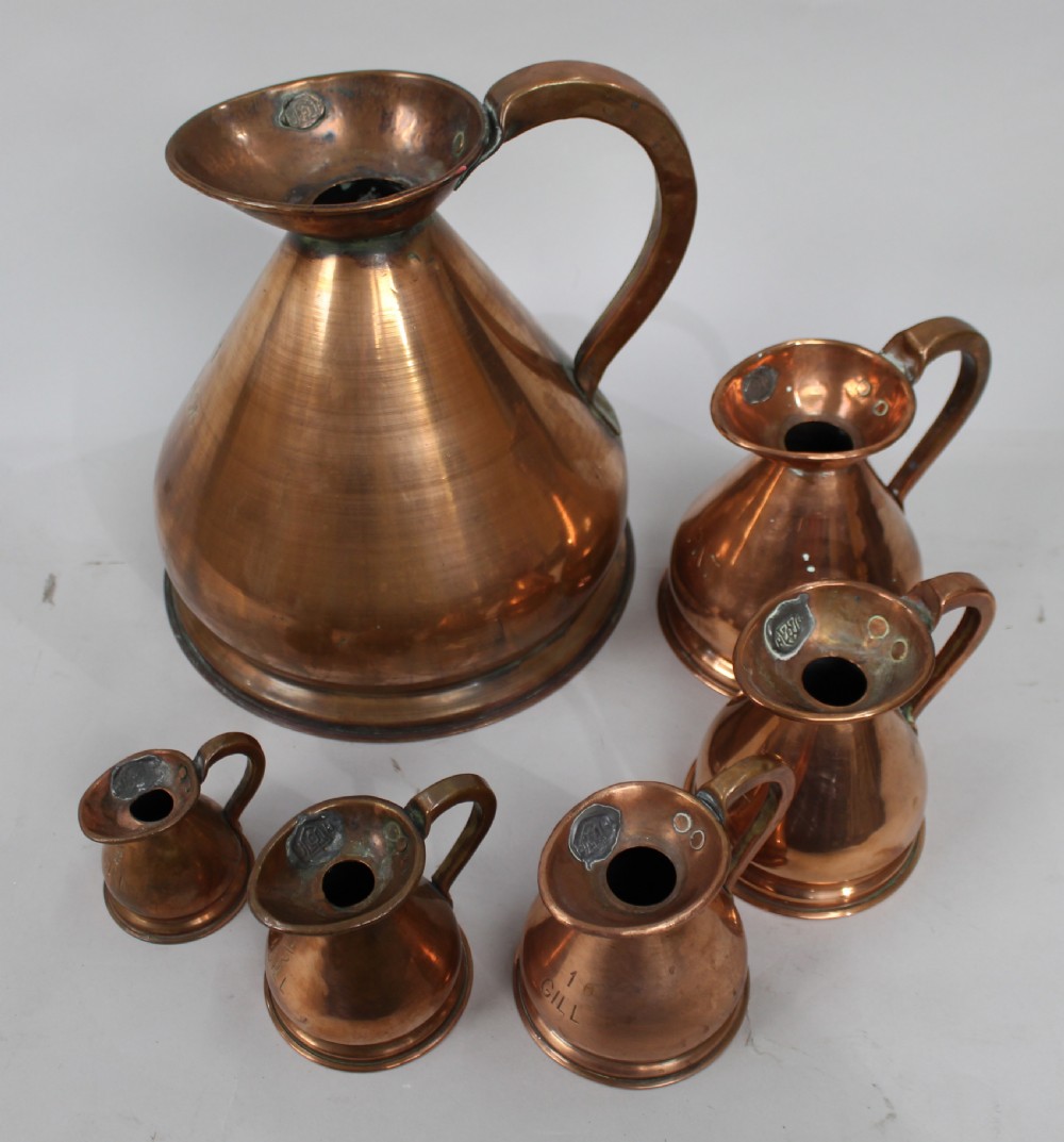 A set of six graduated antique copper haystack liquid measures ranging in size from one gallon down to one eighth gill, arranged on a plain background. View IV