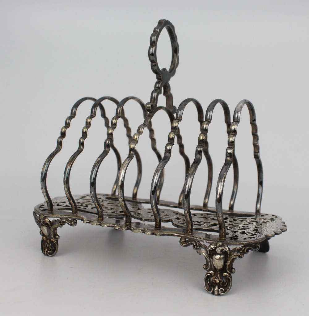 A Victorian silver-plated toast rack with six arched dividers, a central loop handle, a pierced base, and four scrolled feet.