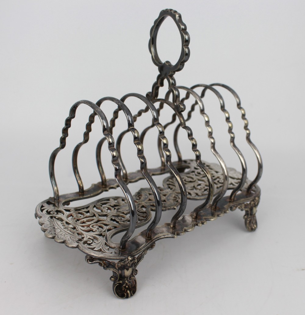 A Victorian silver-plated toast rack with six arched dividers, a central loop handle, a pierced base, and four scrolled feet. View II