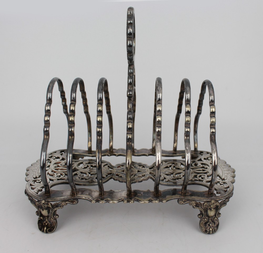 A Victorian silver-plated toast rack with six arched dividers, a central loop handle, a pierced base, and four scrolled feet. View III