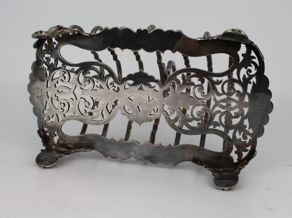 A Victorian silver-plated toast rack with six arched dividers, a central loop handle, a pierced base, and four scrolled feet. View IV