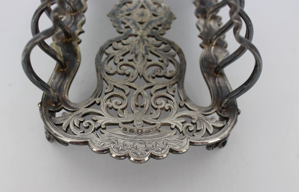 A Victorian silver-plated toast rack with six arched dividers, a central loop handle, a pierced base, and four scrolled feet. View V