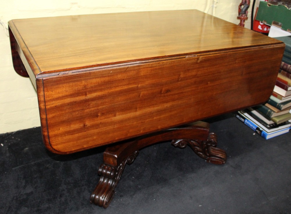 A polished mahogany William IV drop-leaf centre table featuring a rectangular top, drop sides, and a carved pedestal base with scroll feet.