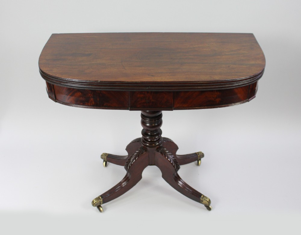 An early nineteenth-century Regency flame mahogany tea table featuring a fold-over top, turned central pedestal column, and four carved splayed legs with brass castors.