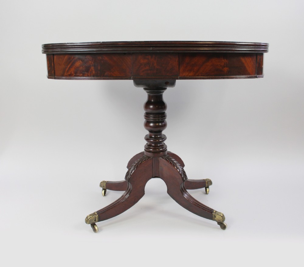 An early nineteenth-century Regency flame mahogany tea table featuring a fold-over top, turned central pedestal column, and four carved splayed legs with brass castors. View III