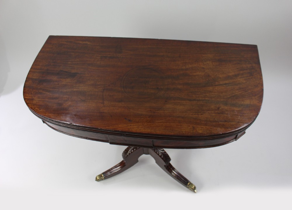 An early nineteenth-century Regency flame mahogany tea table featuring a fold-over top, turned central pedestal column, and four carved splayed legs with brass castors. View IV