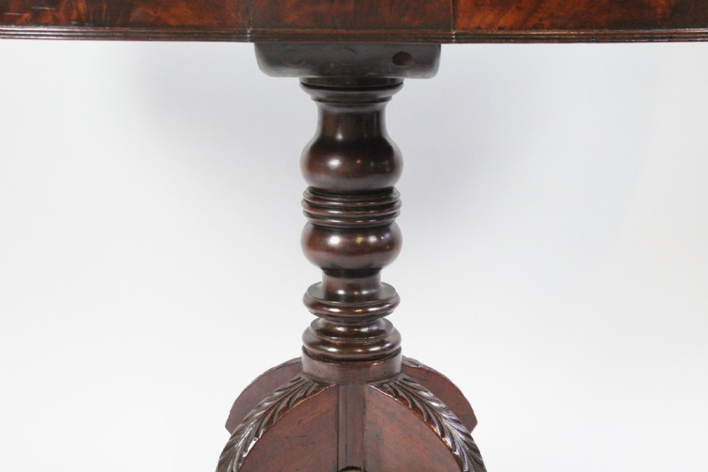 An early nineteenth-century Regency flame mahogany tea table featuring a fold-over top, turned central pedestal column, and four carved splayed legs with brass castors. View VIII