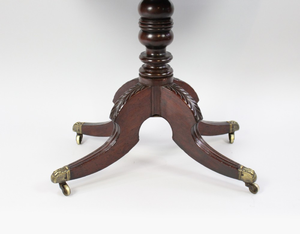 An early nineteenth-century Regency flame mahogany tea table featuring a fold-over top, turned central pedestal column, and four carved splayed legs with brass castors. View IX
